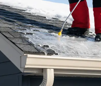 Ice dam removal technician using a steam wand to melt thick ice buildup on a residential roof in Dover, DE
